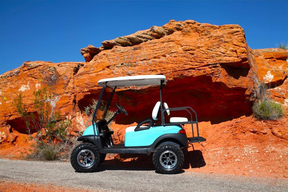 Teal lifted golf cart in front of red rock