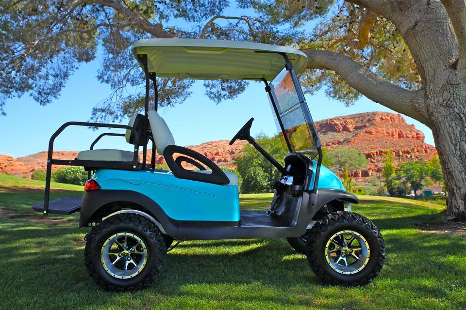 Lifted teal golf cart parked under a tree with red cliffs behind it